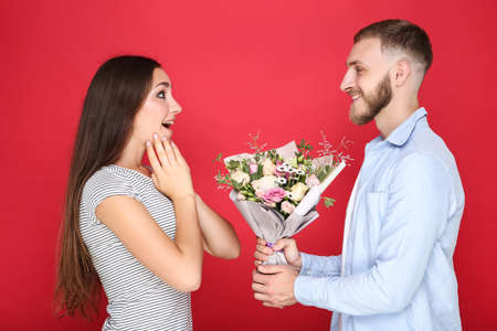 Happy young couple with bouquet of flowers on red backgroundの写真素材