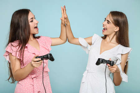 Young happy girlfriends playing computer game with joysticks on blue backgroundの写真素材
