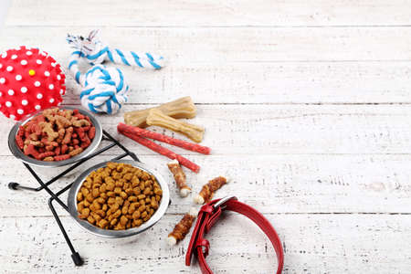 Dry pet food in bowls with collar and toy ball on white wooden tableの写真素材