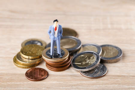 Miniature people with coins on wooden tableの写真素材