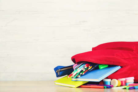 Backpack with school supplies on white wooden background