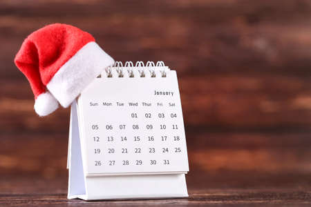 Calendar page with red santa hat on brown wooden backgroundの写真素材