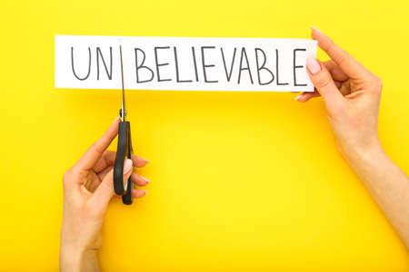 Female hands using scissors for cutting word Unbelievableの写真素材