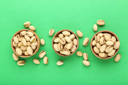 Tasty pistachios in bowls on green backgroundの写真素材