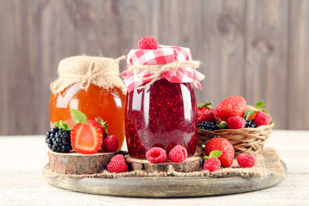 Jam in glass jars with fresh berries on wooden background
