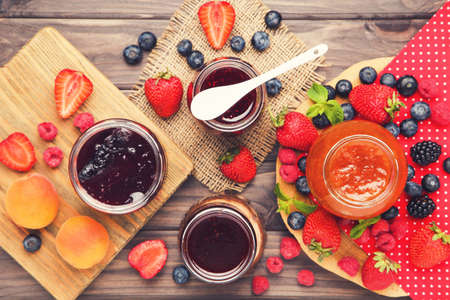 Sweet jam in glass jars with berries on wooden table