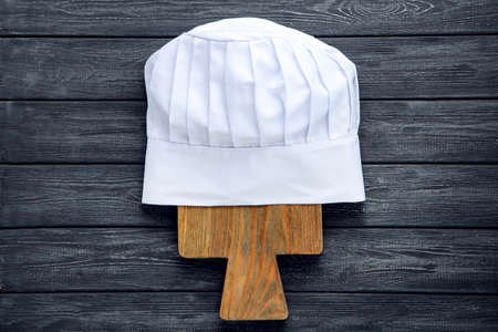 Chef hat with cutting board on black wooden background