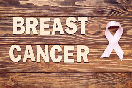 Pink ribbon and inscription Breast Cancer on wooden background