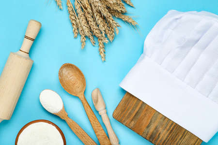 Chef hat with wheat ears, rolling pin, wooden spoons and bowl of flour on blue backgroundの写真素材