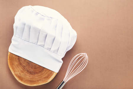 Chef hat on wooden cutting board with pink whisk on brown backgroundの写真素材