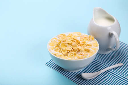 Corn flakes in bowl with milk and jar on blue background
