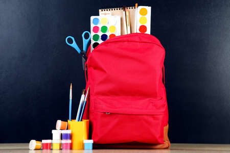 Backpack with school supplies on black background