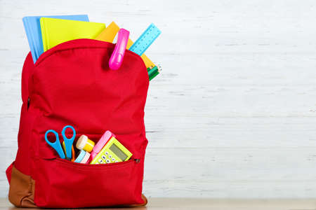 Backpack with school supplies on white wooden background
