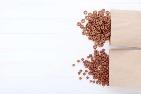 Various chocolate corn flakes with paper bags on white wooden table