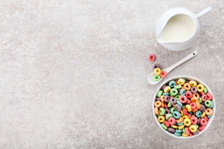 Colorful corn rings with milk in jar and spoon on gray background