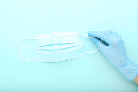 Medicine face mask and female hand in glove on blue background
