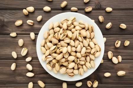 Tasty pistachios in plate on wooden table