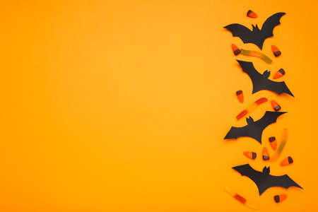 Halloween paper bats with candies on orange backgroundの写真素材