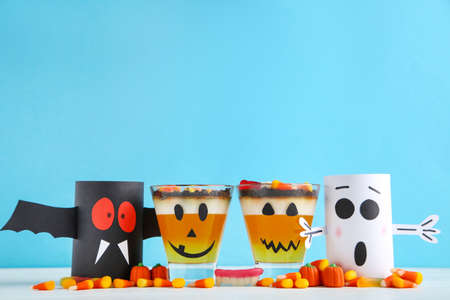 Halloween jelly in glasses with candies and paper ghosts on blue background
