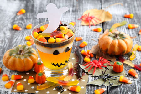 Halloween jelly in glasses with candies, pumpkins and spiders on wooden table