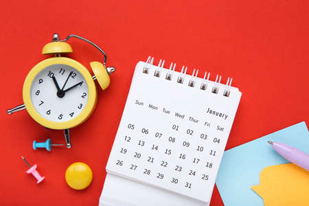 Calendar page with sticky notes and alarm clock on red backgroundの写真素材