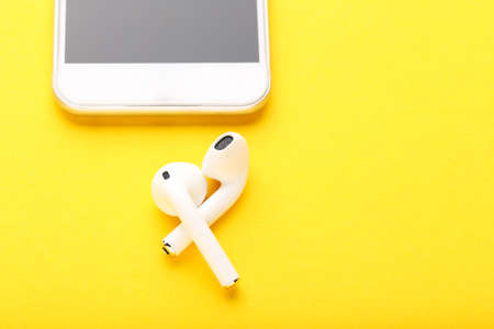 White wireless earphones with mobile phone on yellow backgroundの写真素材