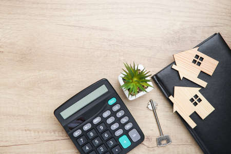 House models with calculator, key, green plant and notepad on wooden table