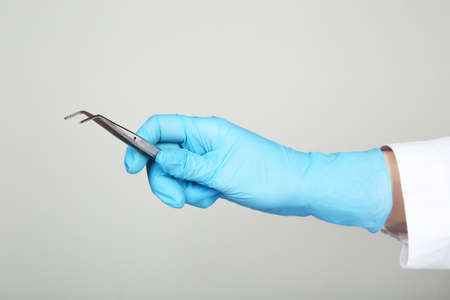 Doctor hand in glove holding dental instrument on gray backgroundの写真素材