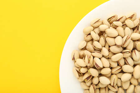 Tasty pistachios in plate on yellow backgroundの写真素材