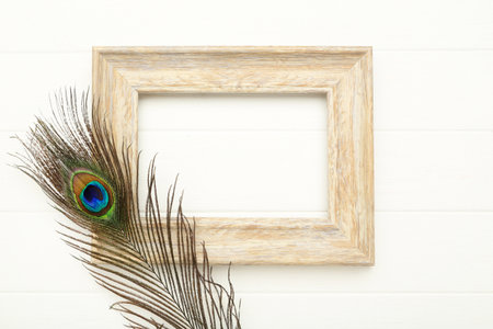 Peacock feather with wooden frame on white wooden tableの写真素材
