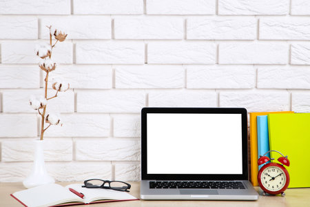Laptop computer with notepads, cotton branch and alarm clock on brick wall background