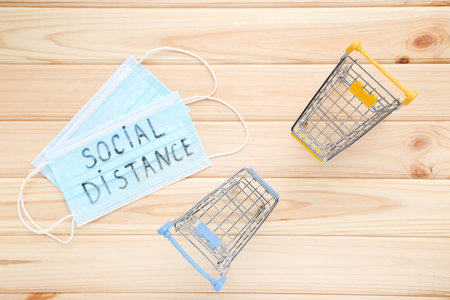 Medicine mask with inscription Social Distance and shopping carts on wooden background