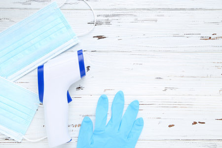 Non-contact infrared thermometer with medical masks and gloves on white wooden background