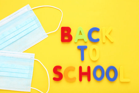 Inscription Back to School and medicine mask on yellow background