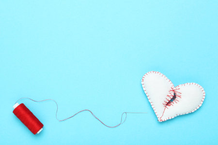 Broken fabric heart with red thread on blue background