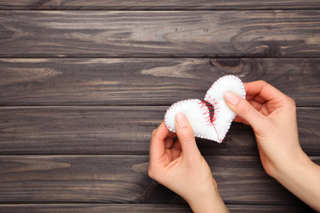 Female hands with broken fabric heart on brown wooden table