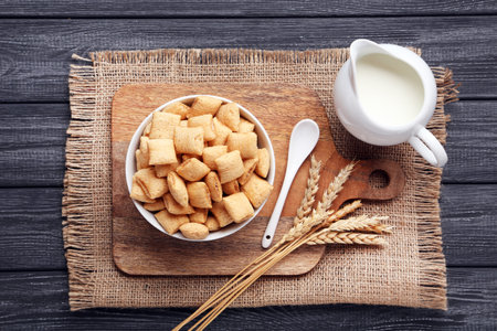 Corn pads with milk in jar and wheat ears on black wooden table