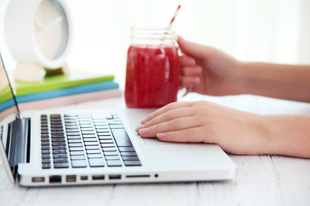 Woman working on laptop and fresh smoothie on white wooden tableの写真素材
