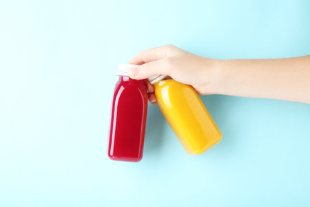 Female hand holding plastic bottles with smoothie on blue background