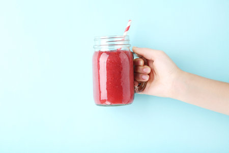 Female hand holding glass jar with red smoothie on blue backgroundの写真素材