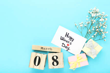 Wooden calendar cubes with gift boxes, gypsophila flowers and text Happy Womens Day on blue...
