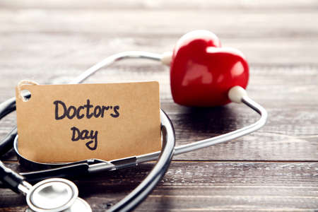 Stethoscope with red heart and text Doctor's Day on wooden tableの写真素材