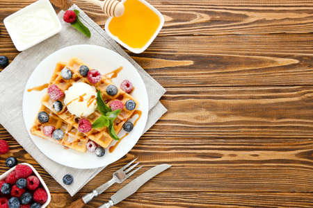 Tasty waffles with fresh berries and ice cream on brown wooden backgroundの写真素材