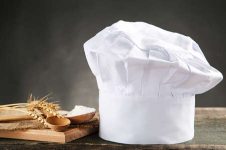 Chef hat with wooden cutting board, flour and wheat ears on black backgroundの写真素材