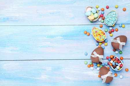 Easter chocolate eggs with candies and sprinkles on blue wooden table