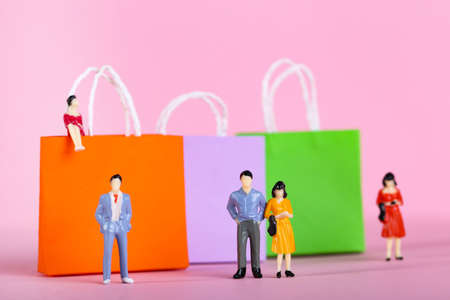 Miniature people with paper shopping bags on pink backgroundの写真素材