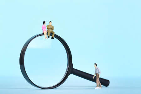 Miniature people with magnifying glass on blue backgroundの写真素材