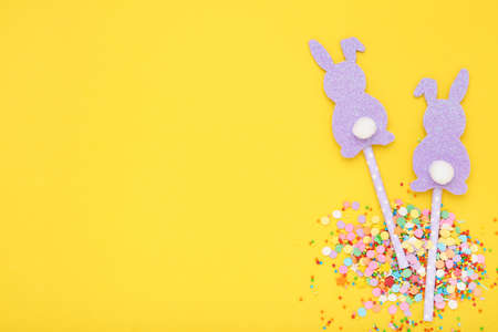 Easter concept. Paper rabbits with colorful sprinkles and confetti on yellow background