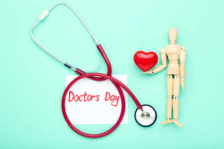 Stethoscope with red heart, wooden figure and text Doctor's Day on mint background