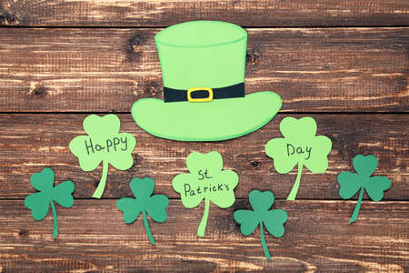 St. Patrick's Day. Paper clover leafs and hat on brown wooden table